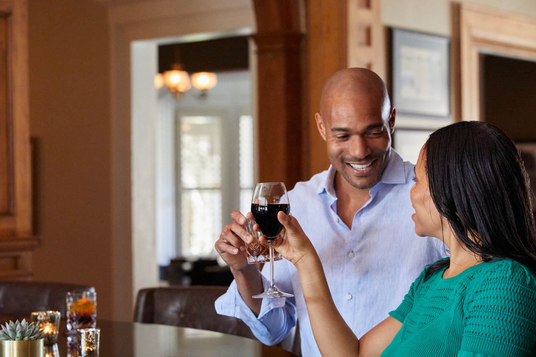 A couple looking into each others eyes at the bar with a cocktail and glass of red wine