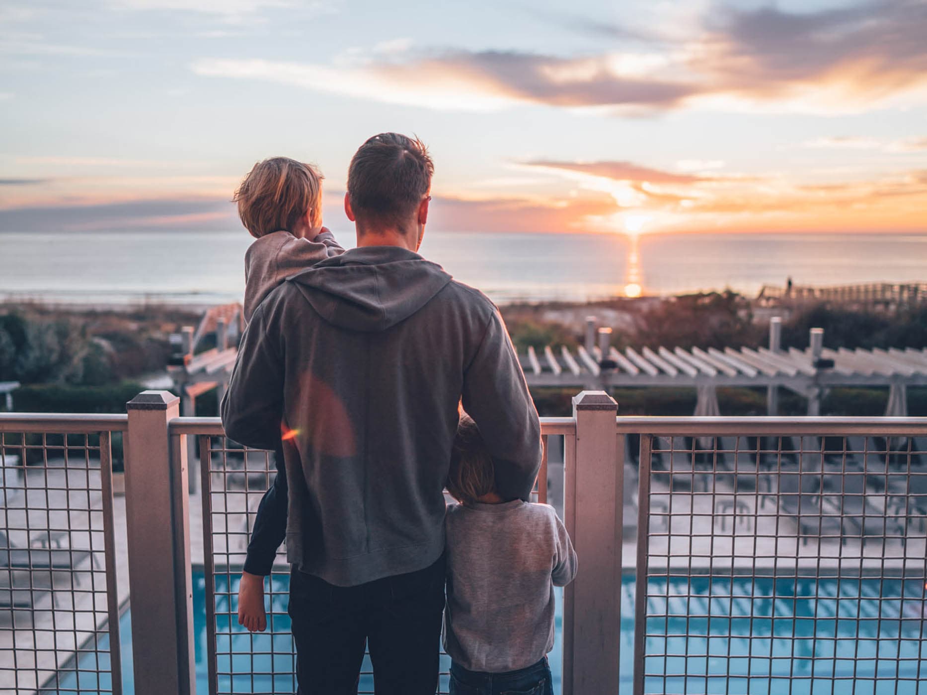 A man on a room balcony with his 2 kids looking at the sunset