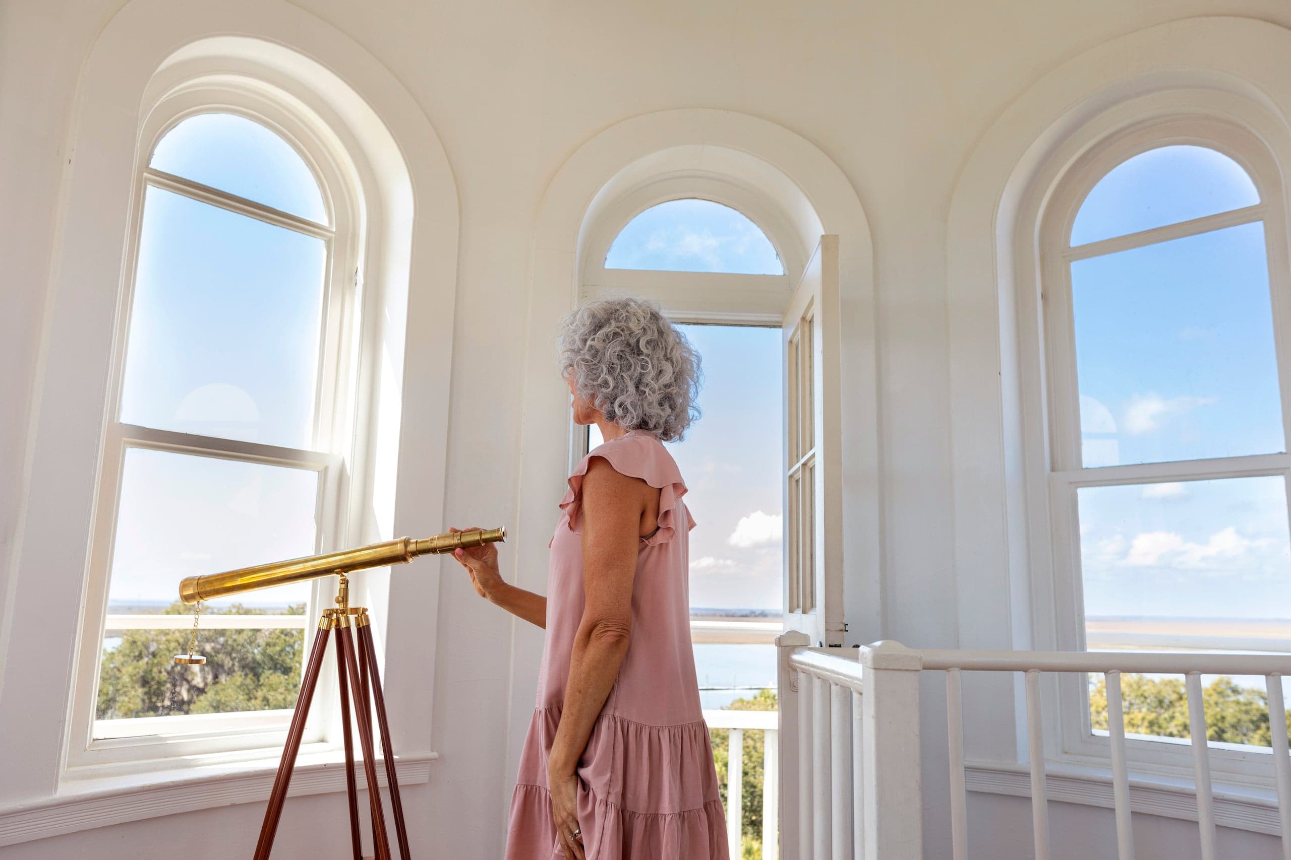 A woman with grey curly long hair and a pink dress in the top observatory room at JIRC