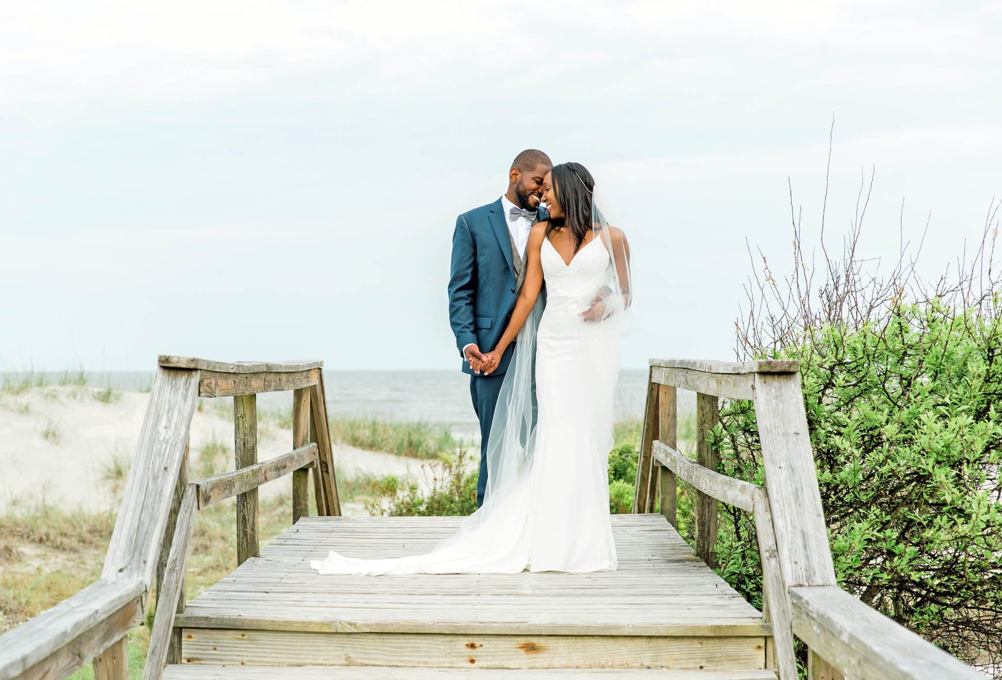 A newly wed couple embracing on the wooden walkway at the beach