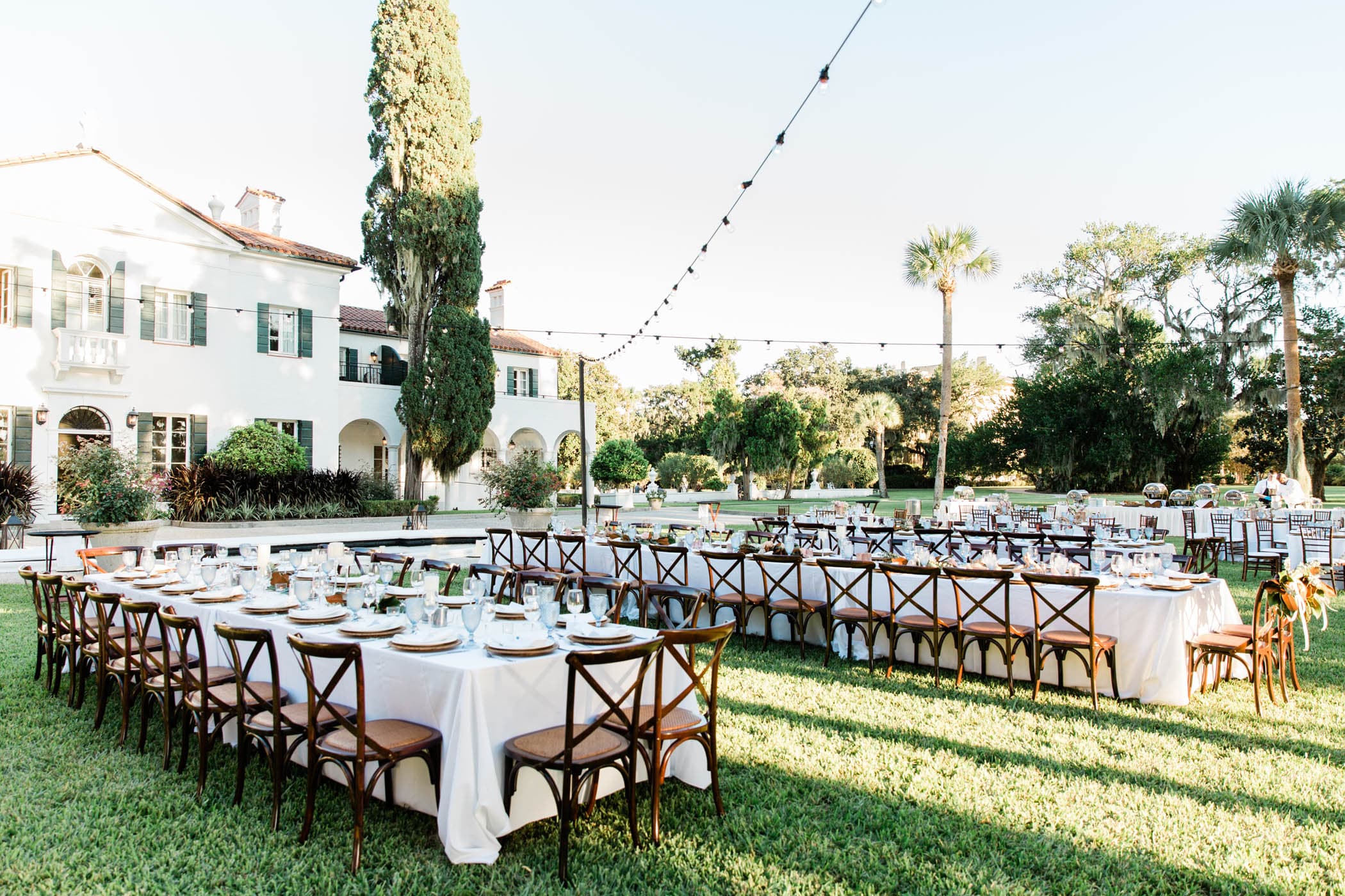 An outdoor wedding set up with 3 long tables with dinnerware and glasses