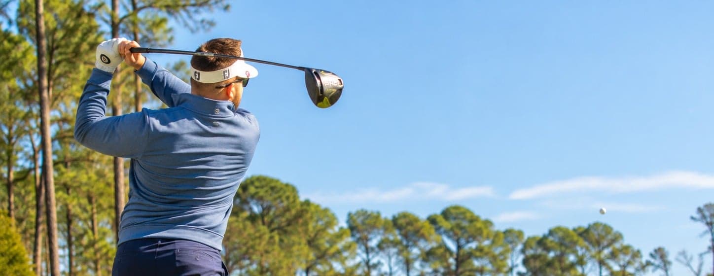 Golfer driving a tee shot down a sunny fairway lined with tall pines on the championship golf course at Jekyll Island Club Resort in Georgia.