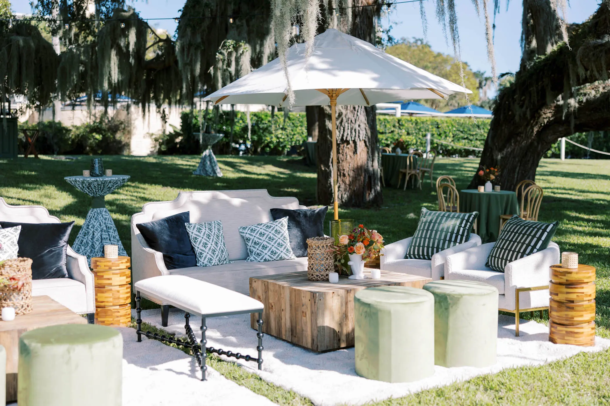 A private outdoor lounge area for a group with comfy couches and chairs, umbrellas to block the sun and a beautiful green space