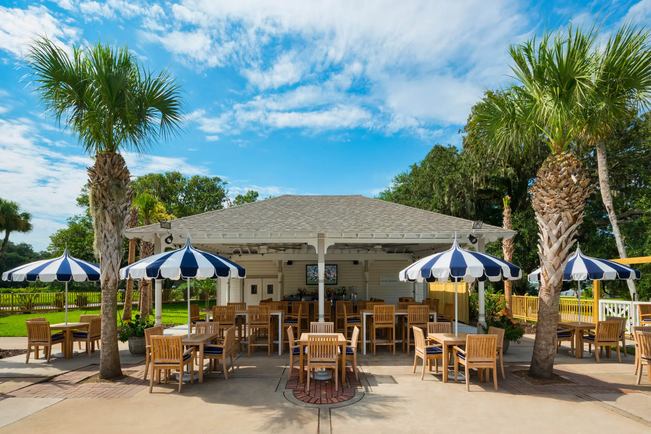 The exterior of the Pool House with plenty of tables and chairs, frames by 2 palm trees