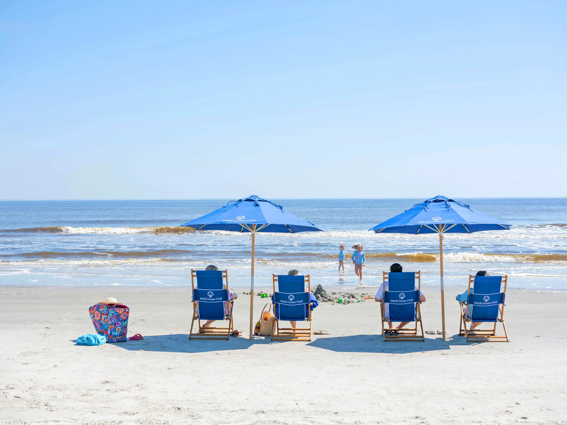 4 people sitting on resort chairs with umbrellas on the beach