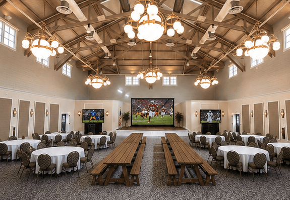 Hospitality Hall with 8 large round tables, 4 large picnic tables, and 3 large TVs