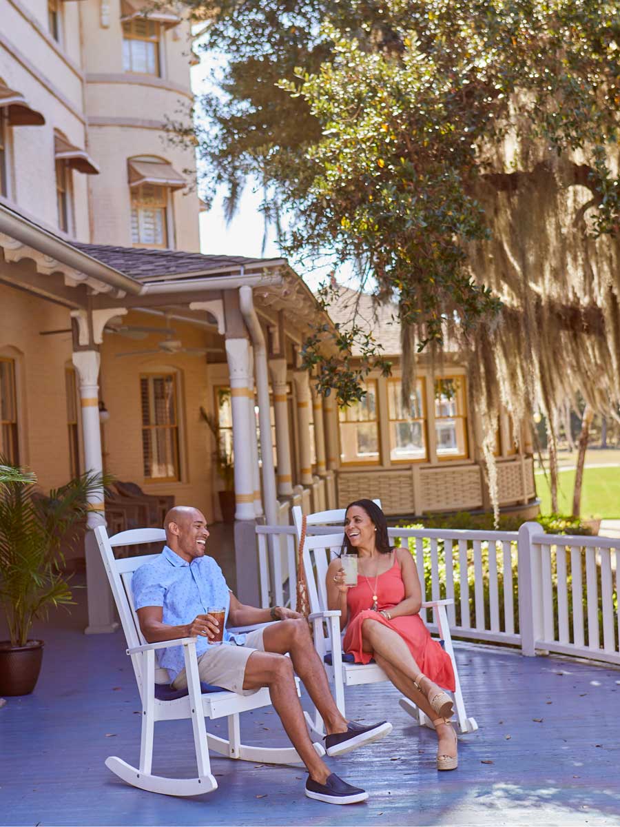 Couple Sitting On The Porch In Rocking Chairs.